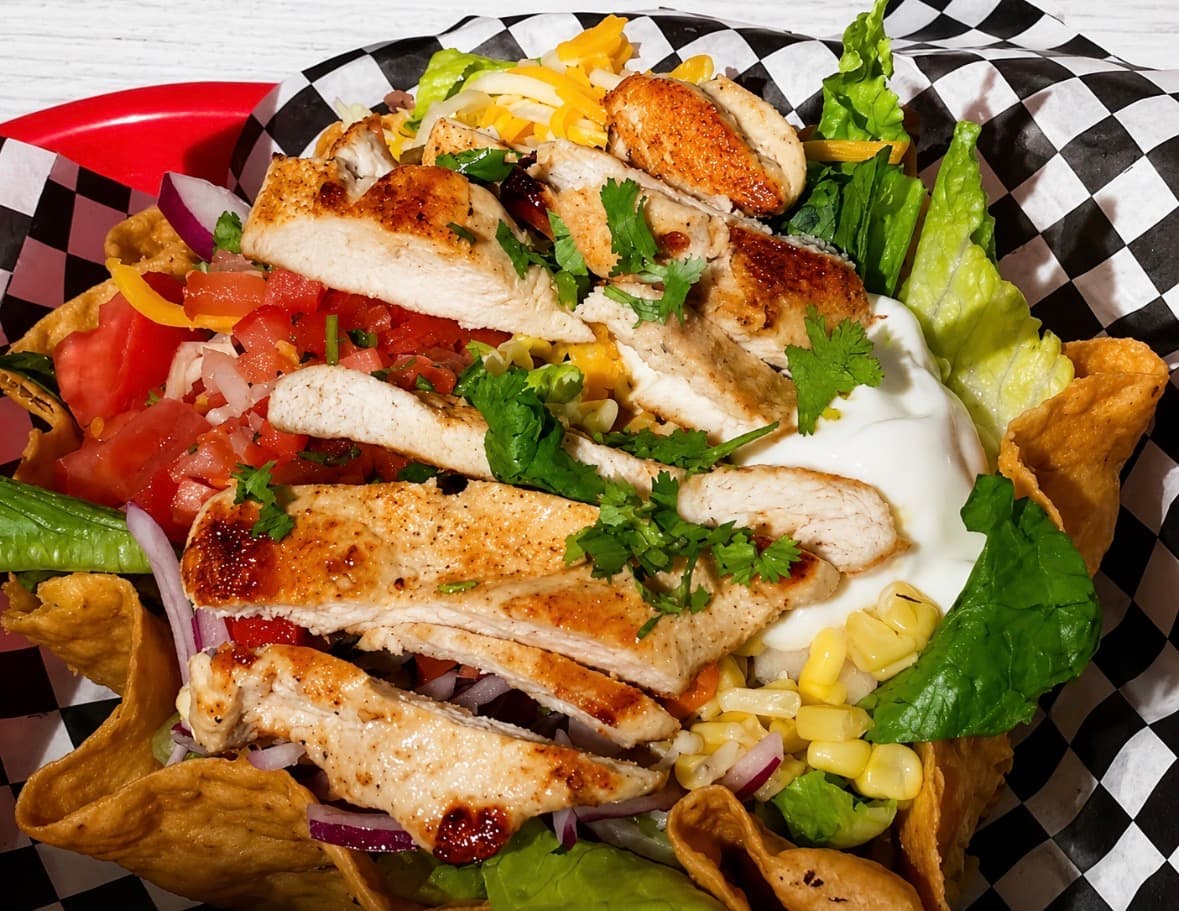 A grilled chicken taco salad in a crisp tortilla bowl